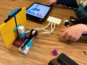 A LEGO SPIKE robot build next to a coding tablet