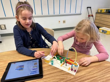 Two homeschool students programming a robot build together at a desk